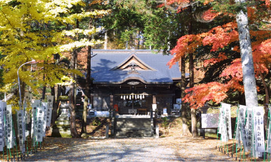 紅葉した紅葉や木々に囲まれ、両脇に義経神社ののぼり旗が並び、入母屋造りの義経神社の外観の写真