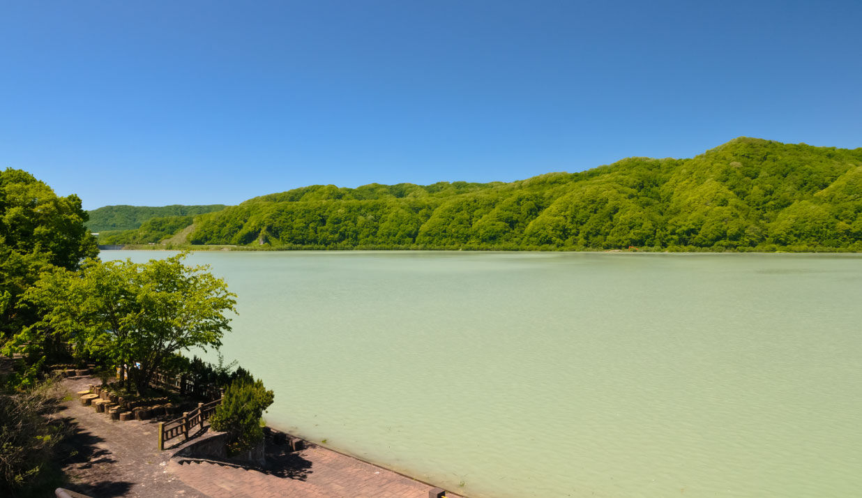 緑が生い茂る山々がそびえたちその手前に流れるエメラルドグリーン色のにぶたに湖の写真