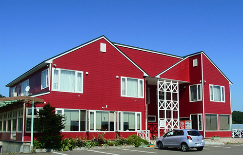 窓を白色の枠で囲まれたウッド調の赤い外壁の建物の写真