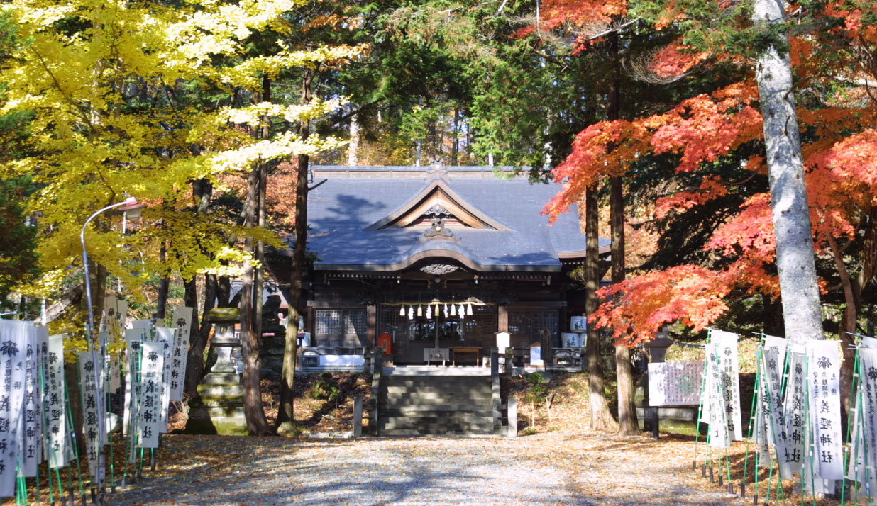 紅葉した紅葉や木々に囲まれ、両脇に義経神社ののぼり旗が並び、入母屋造りの義経神社の外観の写真
