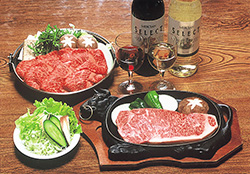 白ワイン、赤ワインと一緒に椎茸や野菜とさしの入った牛肉が並べられた鍋や小皿に盛られたサラダと牛の形をした鉄板の上に置かれたステーキ等が卓上に並べられている写真