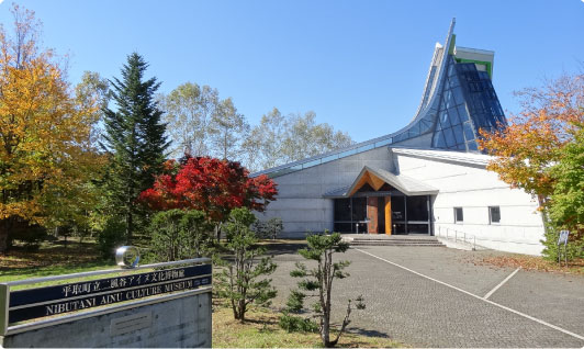 全体的に白の壁で、正面右側が全面ガラス張りの三角形の立方体の窓になって突き出ており、中央が入口になっている二風谷アイヌ文化博物館の写真