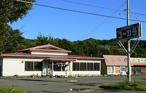 道沿いにドライブインユーカラと書かれた看板とオレンジ色の屋根と白色を基調とした外壁の建物の写真