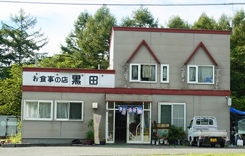 外壁にお食事の店黒田と書かれた白色の看板が設置された2階建ての建物の写真