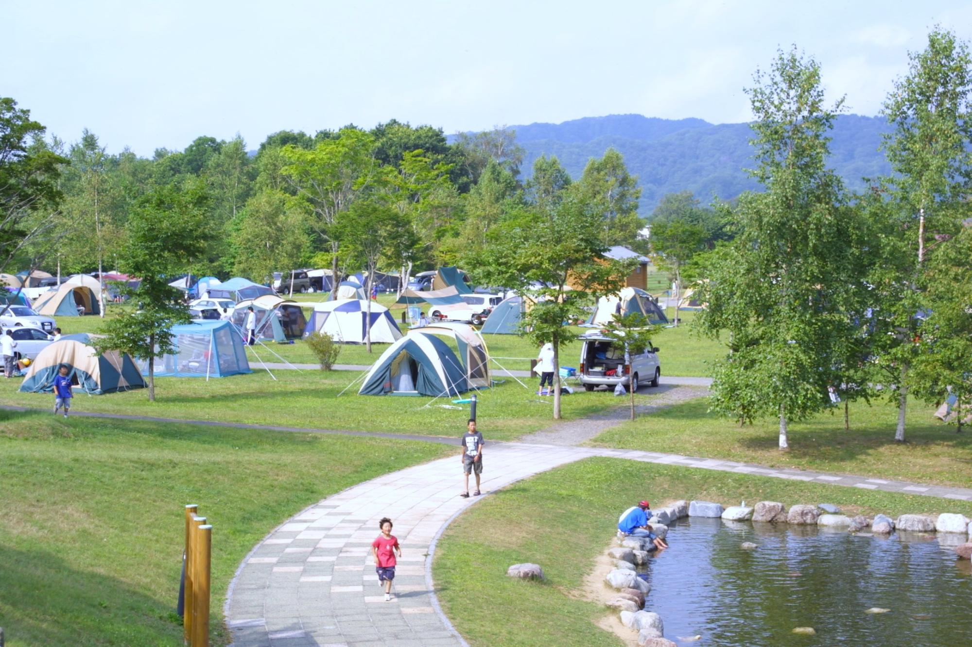 二風谷ファミリーランドキャンプ場に多くのテントが張られており、子どもが手前の散策路を歩いている写真