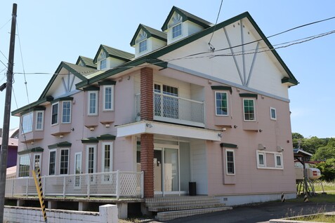 緑色の屋根に白色とピンク色を基調とした外壁で2階建てのホテル駿別館