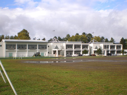 手前に芝生と土のグラウンドがあり、その奥にある白い2階建ての建物の二風谷小学校の外観写真