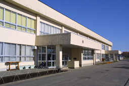 白くて窓が大きい2階建ての建物とその前には道路が写っている平取小学校の入口付近の写真