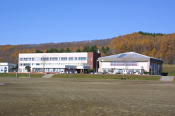 白と茶色の2階建ての長方形の建物と三角屋根をした白い建物が横に並んでいる平取中学校の外観写真