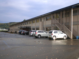 ベージュの2階建ての建物で手前には手すり付きの階段があり、建物の前には車が数台停まっている振内中学校の写真