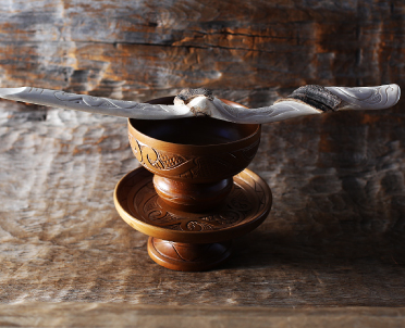 木彫りで出来ているトゥキ（杯）と呼ばれる大小の器を縦に重ね、白く捻じれた形のイクパスイ（捧酒箸）が置かれている尾崎 剛さんの作品写真