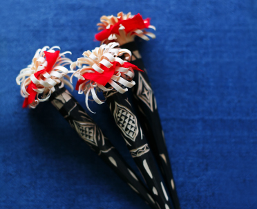 模様が彫られた黒い棒状の先端に赤と白色の彼岸花のような装飾が施されたヘペライの写真