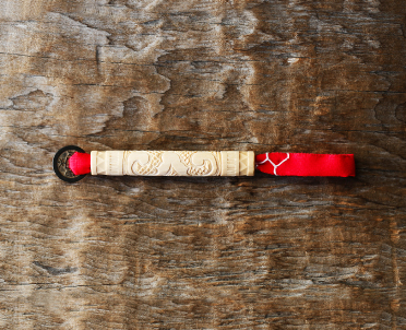 棒状に細く畳まれた赤い布に洲崎さんによって曲線で描かれた文様が彫られた木製の筒が通されたチシポの写真