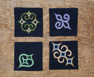 黒地の正方形に緑色や紫色などの色を使い文様がはいっているアイヌ刺繍コースター4枚の写真
